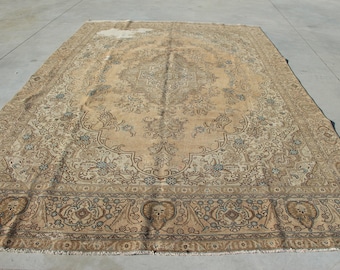 May include: A large rectangular area rug featuring a central medallion design in shades of tan, beige, and light brown. The rug displays intricate floral and vine motifs throughout the field, enclosed by a wide, detailed border with repeating patterns.
