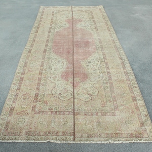 Puede incluir: Una alfombra rectangular de estilo vintage con un diseño central de medallón rosa. La alfombra presenta un fondo color crema con intrincados patrones florales y una apariencia descolorida y desgastada. La alfombra mide aproximadamente 3 metros de largo.