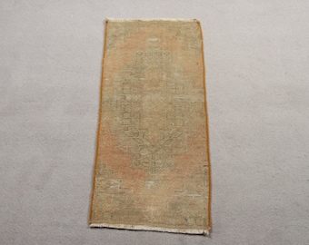May include: A rectangular area rug featuring a faded, muted orange and beige color palette with a central geometric medallion pattern. The rug has a short, worn pile, a distinct orange border along the long sides, and short white fringe at both ends.