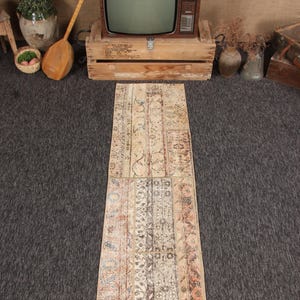 May include: A rectangular, patchwork rug with a distressed, vintage look. The rug features a variety of patterns and colors, including beige, brown, and blue. The rug is approximately 60 inches long and 24 inches wide.