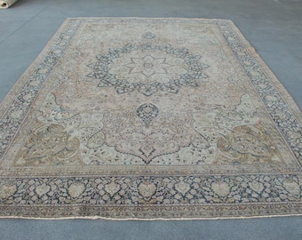 May include: A rectangular area rug featuring a central star-shaped medallion in dark blue and beige. The field is decorated with intricate floral and vine patterns in muted tones of tan, cream, and blue, framed by a wide, detailed floral border.