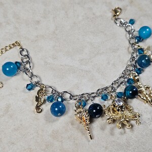 May include: Silver-tone charm bracelet featuring blue beads and gold-tone charms. Charms include a seahorse, starfish, and other sea-themed designs. The bracelet has an adjustable chain for a comfortable fit.