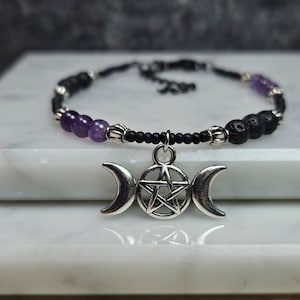 Può includere: Braccialetto con perline nere, perline di ametista e un ciondolo d'argento a forma di tripla luna e pentagramma.