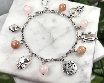 May include: A silver charm bracelet with pink and brown beads, a heart charm, a skull charm, a music note charm, a lyre charm, a constellation charm, and a snake charm.
