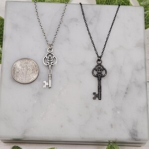 Puede incluir: Dos collares con llaves de plata, uno con una cadena negra y otro con una cadena plateada. Las llaves son ornamentadas y tienen un aspecto vintage.