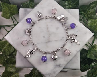 May include: A silver charm bracelet with purple and pink beads, a heart charm, a rose charm, a butterfly charm, and a cupid charm.