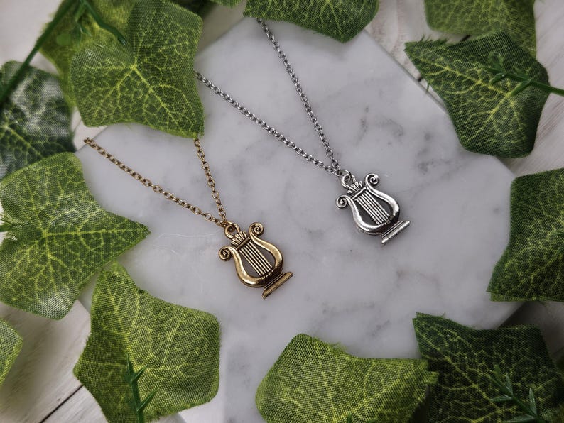 Op de afbeelding: Twee zilveren kettingen met een lier hanger. E&eacute;n ketting is goud en de andere is zilver.