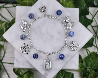 May include: A silver charm bracelet with blue gemstone beads and various silver charms, including a crown, a tree, a couple, and a bird.