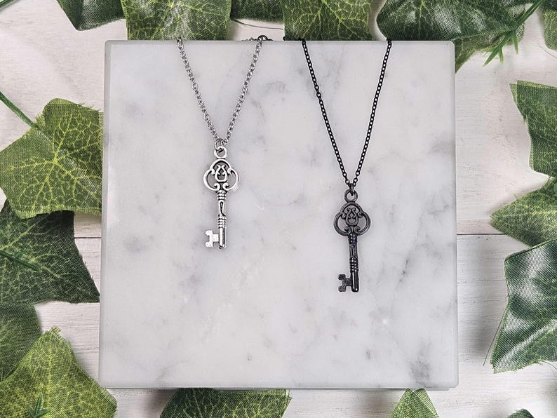 Puede incluir: Dos collares con llaves de plata, uno con una cadena de plata y otro con una cadena negra. Ambas llaves tienen un dise&ntilde;o adornado.