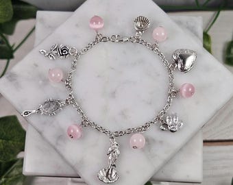 May include: A silver charm bracelet with pink beads and various charms, including a rose, a heart, a seashell, a mirror, a mermaid, and a flower.