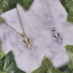 May include: Two necklaces with trident pendants. One necklace has a gold trident pendant and the other has a silver trident pendant.
