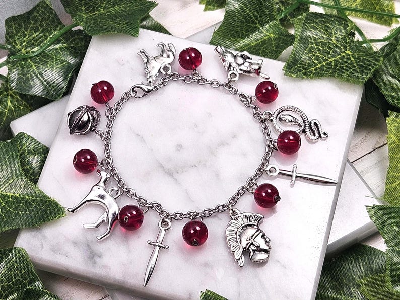 Puede incluir: Un brazalete de plata con cuentas de vidrio rojas y varios dijes de plata, incluyendo una serpiente, una espada, una corona, un lobo y un casco de guerrero.