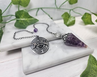 May include: A silver chain pendulum with a purple amethyst crystal point and a silver charm featuring a triple moon and pentagram design.