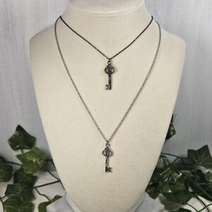 Puede incluir: Un collar de plata con dos colgantes de llave. El collar est&aacute; formado por dos cadenas, una plateada y una negra.