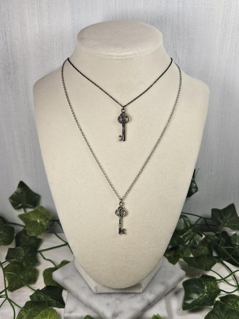 Puede incluir: Un collar de plata con dos colgantes de llave. El collar est&aacute; formado por dos cadenas, una plateada y una negra.