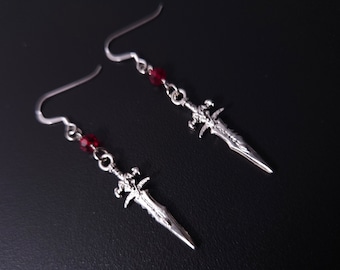 May include: Silver sword earrings with red crystal accents. The swords have a detailed design and are hanging from silver hooks.