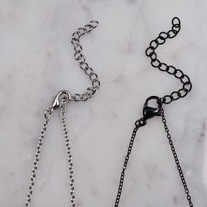Puede incluir: Dos cadenas plateadas con cierres de langosta. Una cadena es plateada y la otra es negra.