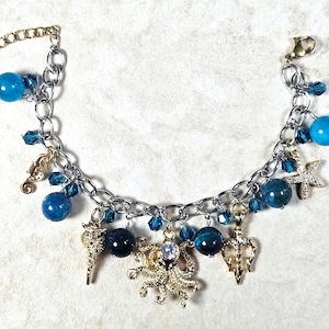 May include: Silver-tone charm bracelet featuring blue beads and sea-themed charms. The bracelet includes a seahorse, starfish, and octopus charm, with a gold-tone chain and clasp. The bracelet is adorned with blue crystal accents.