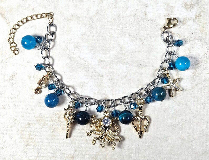 May include: Silver-tone charm bracelet featuring blue beads and sea-themed charms. The bracelet includes a seahorse, starfish, and octopus charm, with a gold-tone chain and clasp. The bracelet is adorned with blue crystal accents.