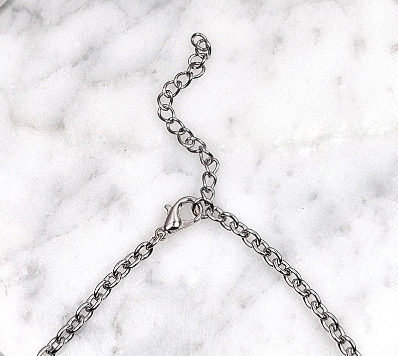 May include: Silver-toned necklace chain with a lobster clasp and adjustable extender. The chain is composed of small, oval links. The background is a white and gray marble pattern.