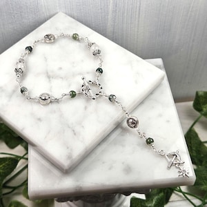 May include: A silver chain bracelet with green and white beads and a silver charm. The bracelet has a toggle clasp.
