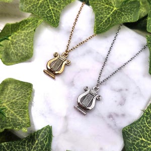 Op de afbeelding: Twee kettingen met lier hangers. De ene ketting heeft een gouden lier hanger, de andere een zilveren lier hanger.