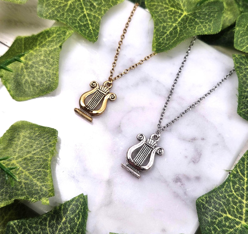 Op de afbeelding: Twee kettingen met lier hangers. De ene ketting heeft een gouden lier hanger, de andere een zilveren lier hanger.