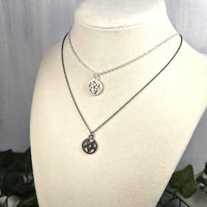 May include: Two silver necklaces with a pentagram pendant. The top necklace is silver and the bottom necklace is black.
