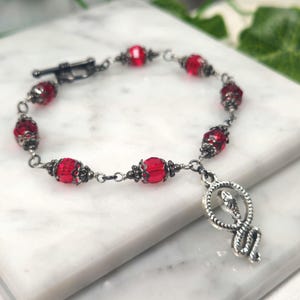 May include: A silver snake charm bracelet with red glass beads. The bracelet has a silver clasp and is made of a delicate chain.