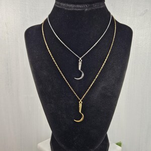 May include: Two necklaces on a black display stand. One necklace is silver, the other is gold. Each necklace has a crescent moon pendant. The gold necklace is slightly longer than the silver one.