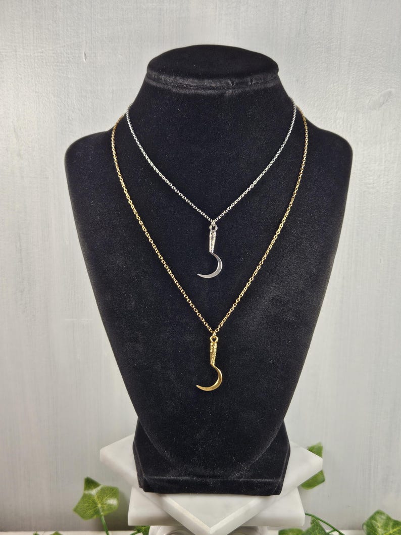 May include: Two necklaces on a black display stand. One necklace is silver, the other is gold. Each necklace has a crescent moon pendant. The gold necklace is slightly longer than the silver one.