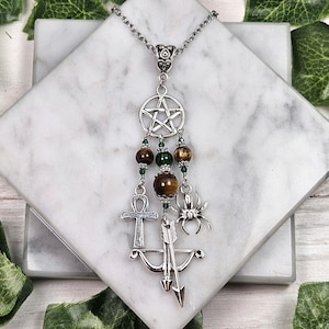 May include: A silver chain necklace with a pentagram charm, tiger eye beads, and other charms including a spider, an ankh, and an arrow.