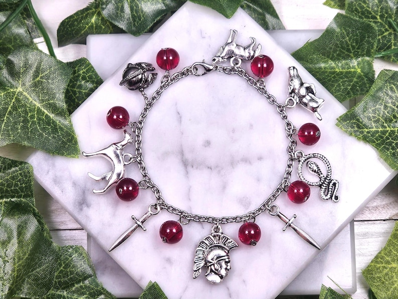 Puede incluir: Un brazalete de plata con cuentas de vidrio rojas y varios dijes de plata, incluyendo una espada, una serpiente, un perro, un casco y un escarabajo.