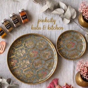 May include: Two round plates with a grey base, gold-toned lattice pattern, and floral motifs. Included are four small glass spice jars with black labels, a copper-toned slotted spatula, and two gold-toned bowls filled with pink dried flowers.