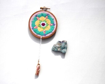 Bordado en bastidor con mandala de sanación en tonos pastel, cristal de rodonita y arte de energía protectora.