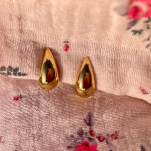Peut inclure: Une paire de boucles d'oreilles en forme de goutte d'or. Les boucles d'oreilles sont petites et délicates.