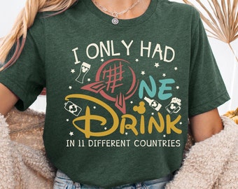Puede incluir: Una camiseta verde con el texto "I only had one drink in 11 different countries" y un gráfico de una cabeza de Mickey Mouse con una jarra de cerveza y un pretzel.