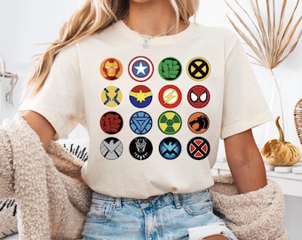 Może przedstawiać: Biała koszulka z nadrukiem graficznym różnych logo superbohaterów Marvela, w tym Iron Mana, Kapitana Amerykę, Hulka, Wolverine'a, Thora, Spider-Mana i innych.