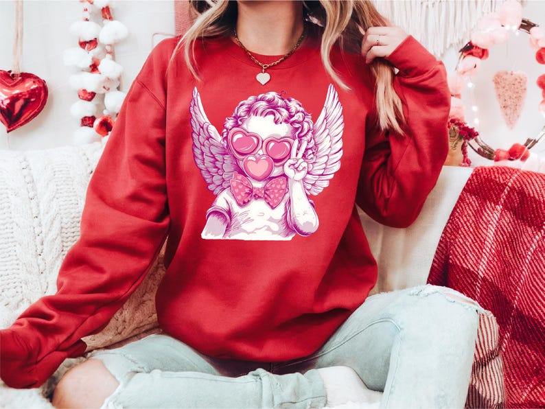 a woman sitting on a couch wearing a red sweatshirt with an angel on it