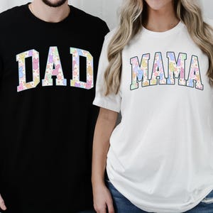 May include: Two black and white t-shirts with the words "DAD" and "MAMA" in a colorful pastel pattern. The shirts are worn by two people.