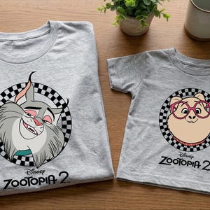 two gray t-shirts with cartoon animal designs, specifically featuring a cat and a dog, along with the text "Disney Zootopia 2".