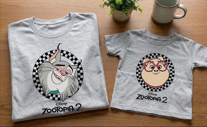 two gray t-shirts with cartoon animal designs, specifically featuring a cat and a dog, along with the text "Disney Zootopia 2".