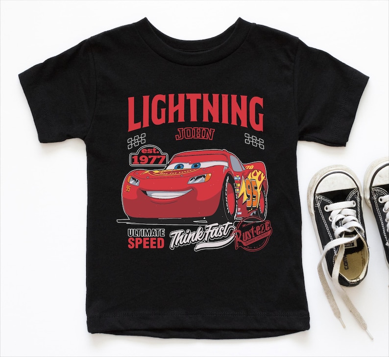 A black t-shirt with a graphic design featuring a red car and the text "Lightning John" along with other text and logos related to the Disney Pixar movie Cars.