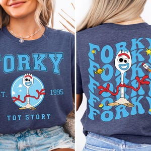 May include: A navy blue t-shirt with a blue and white graphic of the character Forky from Toy Story. The front of the shirt says "Forky" in blue letters with "Est. 1995" and "Toy Story" below. The back of the shirt has a repeating pattern of the word "Forky" in blue with a graphic of Forky in the center.