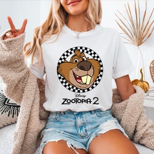 A woman wearing a white t-shirt with a cartoon character and the text "Disney Zootopia 2" printed on it.