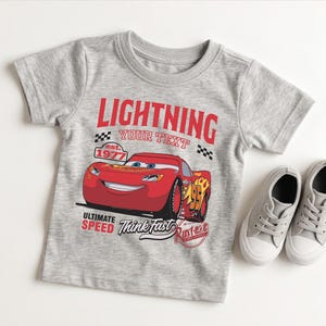 A gray t-shirt with a red and yellow design featuring a cartoon car and the text "Lightning" and "Your Text" printed on it.