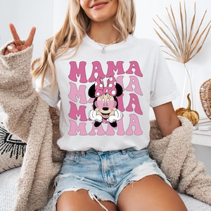 May include: White t-shirt with a pink and white graphic of Minnie Mouse wearing sunglasses and the word "MAMA" repeated multiple times.