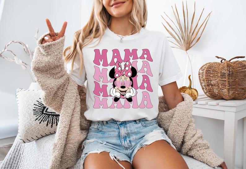 May include: White t-shirt with a pink and white graphic of Minnie Mouse wearing sunglasses and the word "MAMA" repeated multiple times.
