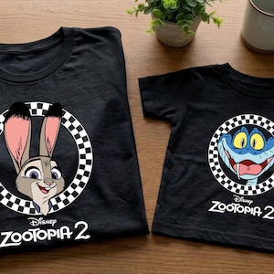 two black t-shirts with cartoon rabbit characters and the text "Disney Zootopia 2" printed on them, along with a small potted plant and a coffee mug in the background.
