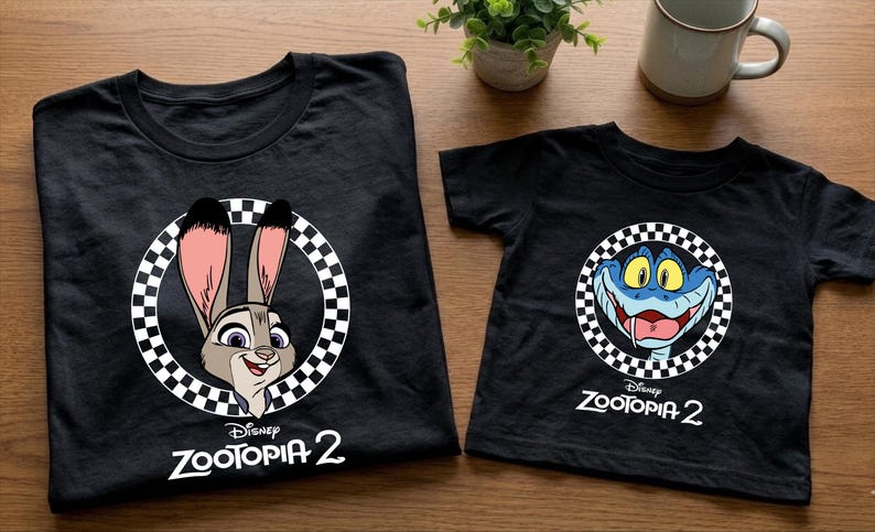 two black t-shirts with cartoon rabbit characters and the text "Disney Zootopia 2" printed on them, along with a small potted plant and a coffee mug in the background.